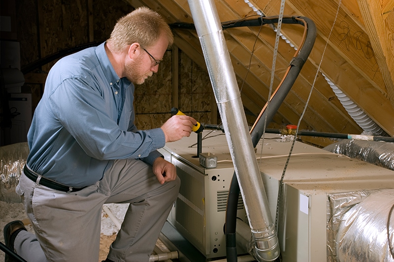 HVAC technician working on unit in a homes attic.