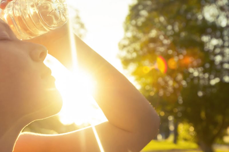 Woman outside in the heat, using water bottle to cool down.