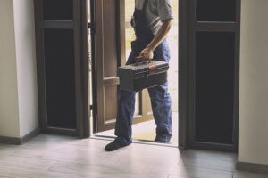 HVAC technician walking into a home carrying a tool box ready to perform service.