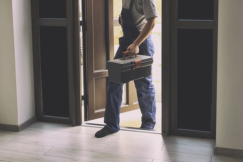 HVAC technician walking into a home carrying a tool box ready to perform service.