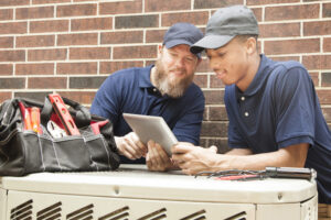 Two air conditioner repairmen working on a homes HVAC unit and using a digital tablet.